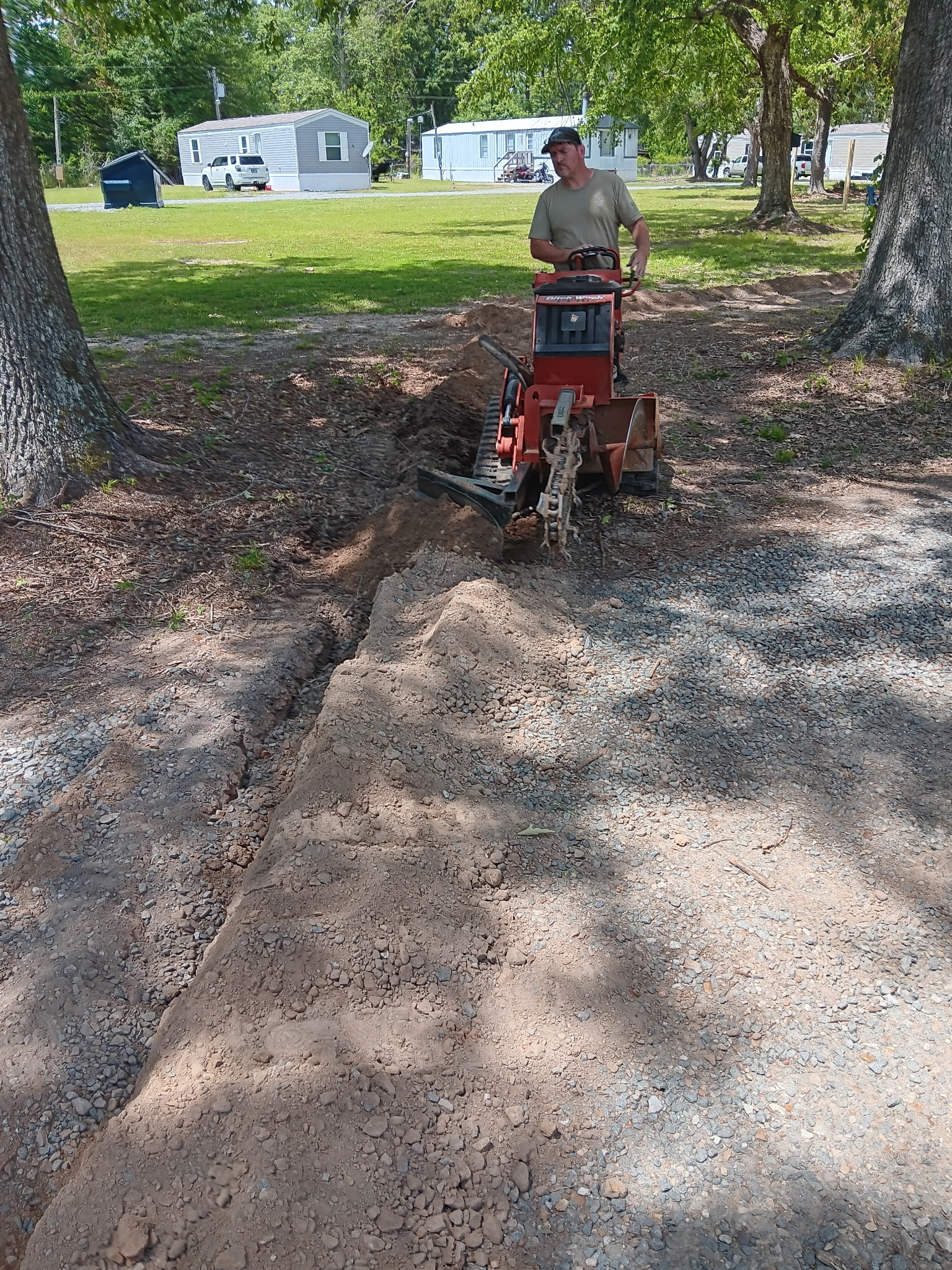 Crew operating Ditch Witch trencher between trees, McKinney, TX
